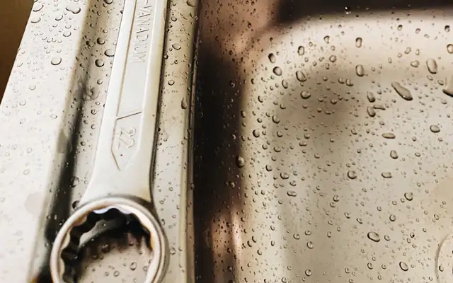 Wrench resting in a stainless steel sink with water droplets